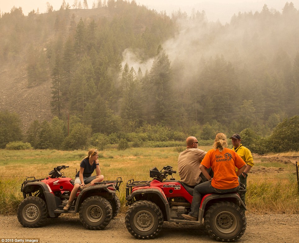 Residents confer with a firefighter while keeping an eye on a blaze on a hillside near Omak, Washington, on Sunday afternoon
